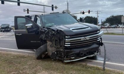 Black Chevrolet Silverado 3500 HD pickup truck with severe front-end collision damage, photographed at intersection with traffic lights overhead.