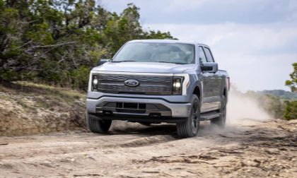 Silver Ford F-150 Lightning electric pickup truck driving off-road on rugged trail