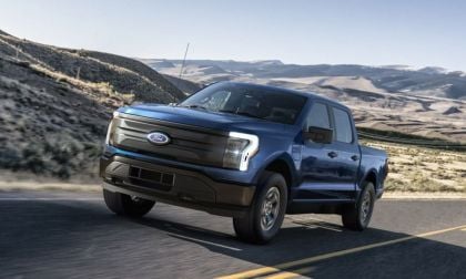 Blue Ford F-150 Lightning electric truck driving on mountain highway with rugged terrain backdrop
