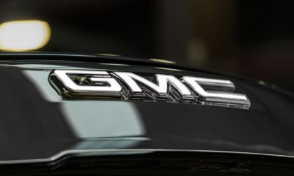 Close-up of a shiny chrome GMC logo on a Sierra EV surface, conveying a sense of luxury and modernity with soft, blurred lighting in the background.