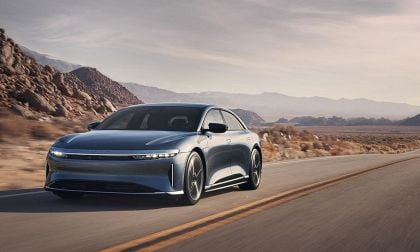 A Gray 2025 Lucid Air drives along a winding road, surrounded by rugged mountains and a vast desert landscape under a clear sky.