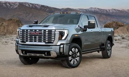 A silver GMC truck parked in a desert landscape, showcasing its bold grille and rugged design against a mountainous backdrop.