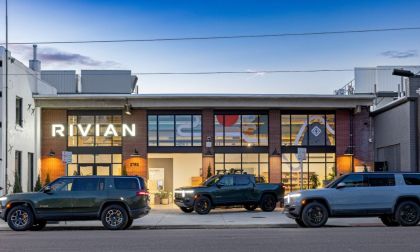 Rivian R1T and R1S electric vehicles parked outside a Rivian showroom at dusk.