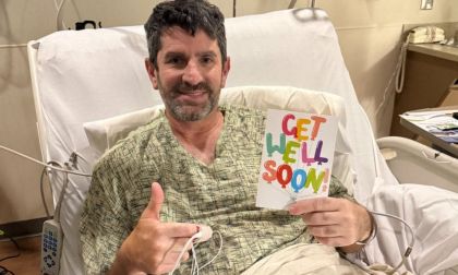 Jack's dad in a hospital bed smiles, holding a colorful "Get Well Soon" card. He gives a thumbs-up with his other hand. The mood is positive and hopeful.