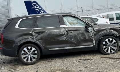 Jenni's black 2020 Kia Telluride with significant side damage and a deflated airbag visible in the driver's window, parked in a gravel lot near other vehicles and fencing.