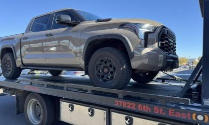 A tan 2025 Toyota Tundra with rugged tires is secured on a flatbed tow truck under a clear blue sky. The scene conveys a sense of utility and readiness.