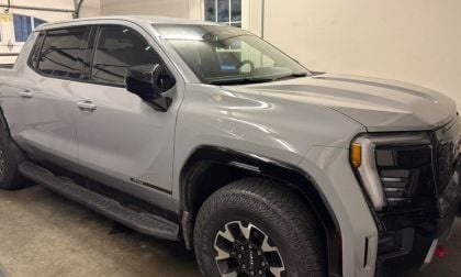 A grey GMC Sierra EV parked in a garage. The truck has large tires and tinted windows, conveying a rugged yet modern design.