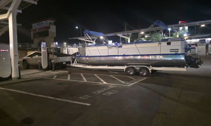 A boat is being towed by a Tesla Cybertruck parked in a charing station at night, the scene is illuminated by overhead lighting.