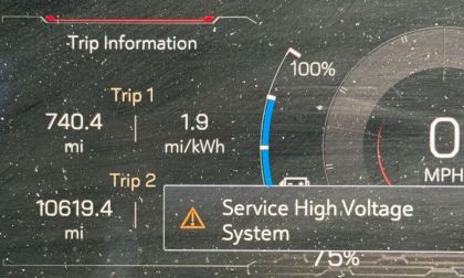 Dashboard of a GMC Sierra EV displaying trip information with a "Service High Voltage System" warning. Shows Trip 1 at 740.4 miles, efficiency 1.9 mi/kWh, and battery at 100%.