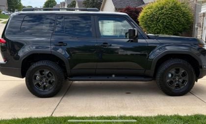 Black Lexus GX 550 SUV parked on suburban driveway, side profile with rugged off-road tires and dark alloy wheels