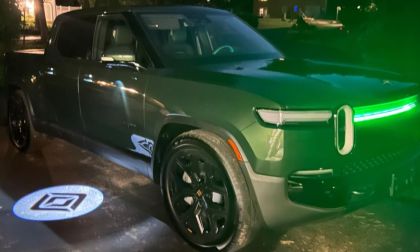 Green Rivian R1T electric truck parked at night with glowing green headlights and branded logo projection on ground