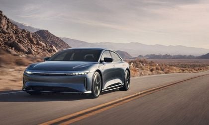 A sleek Lucid Air driving along a winding road with rocky mountains and a hazy sky in the background.