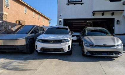 Three electric cars parked on a driveway: a Tesla Cybertruck is on the left, a white Honda Prologue in the middle, and a sleek gray Genesis on the right. A modern house and open garage are in the background.