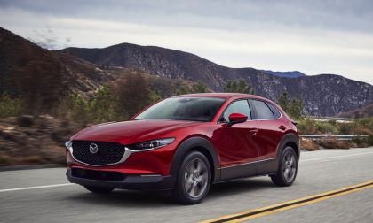 Red Mazda CX-30 compact SUV driving on a scenic mountain road, front three-quarter exterior view