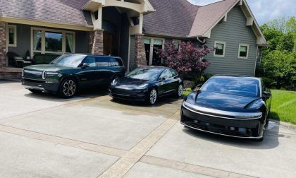Three electric cars, Rivian, Tesla Model 3, and Lucid Air—are parked in a sunny driveway beside a modern house.