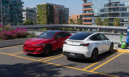 Red Ford Mustang Mach-E and a white Tesla Model Y parked in a city parking.