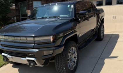 A black GMC Hummer EV truck with chrome accents and large tires is parked in a driveway. Sunlight reflects off the polished surface, creating a bold and powerful look.