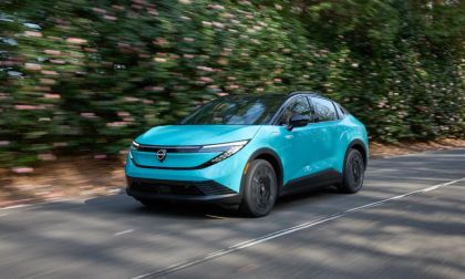 2026 Nissan LEAF electric vehicle driving on a tree-lined road, front three-quarter motion view.