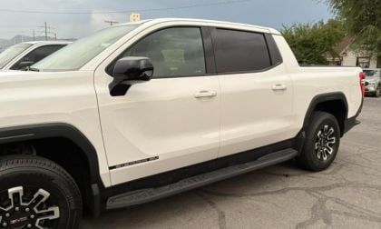 A white GMC Sierra EV truck parked, featuring sleek curves, dark rims, and tinted windows under a cloudy sky