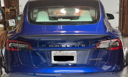 Blue Tesla Model 3 with a Porsche badge instead of the Tesla logo. Car is seen from the rear in a garage, the Dual Motor label is visible, reflecting a playful tone.