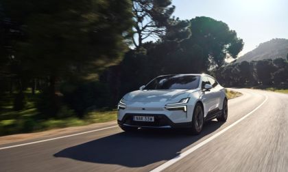 White electric SUV driving on curved mountain road surrounded by pine trees