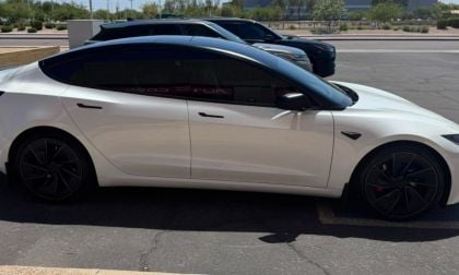 White Tesla Model 3 with black roof and wheels, side profile in parking lot with arid landscape background