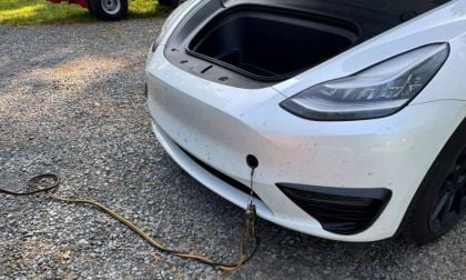 A white Tesla Model Y with the frunk open and cable attached during battery replacement process