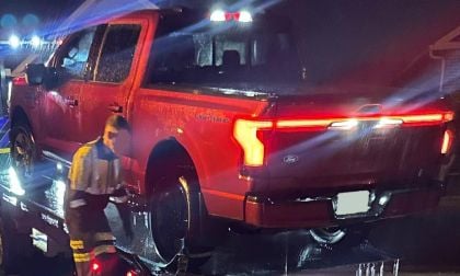 A red Ford truck is being loaded onto a tow truck at night, with rain falling and emergency lights flashing in the background.