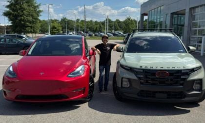 Riley is seen standing and smiling between a red Tesla and a sage gray Hyundai Santa Cruz in a car dealership lot on a sunny day, conveying excitement and choice.
