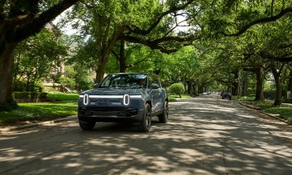 Rivian R1S electric SUV driving along a tree lined residential street in a suburban neighborhood