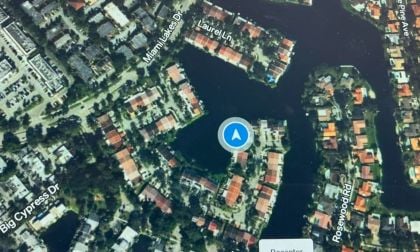 Aerial view of waterfront neighborhood with red-roofed houses, blue navigation marker, and winding water channels between residential areas.