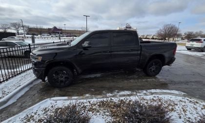 A black Ram 1500 pickup truck parked next to a metal railing in a snowy parking lot.