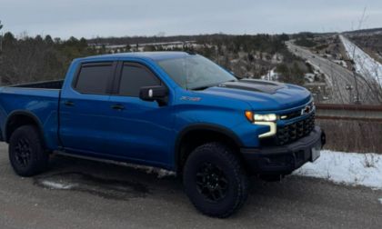 Bright blue Chevrolet Silverado ZR2 pickup truck with black wheels parked on snowy roadside with highway backdrop