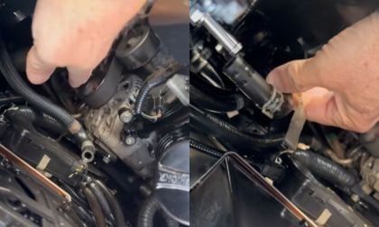 Close-up view of hands performing mechanical work on an engine, showing various hoses, connectors and engine components in a dark engine bay.