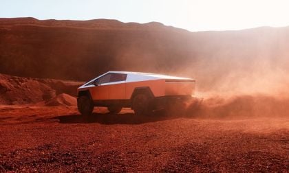 Tesla Cybertruck accelerating through dusty desert terrain with rugged mountains in background