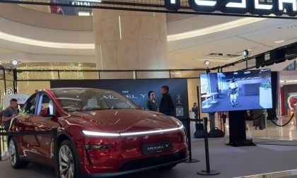 A red Tesla Model Y is showcased in a modern mall setting, with a digital screen displaying a robotic character beside it.