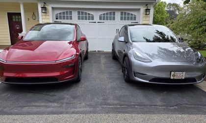 A red Tesla Model Y Juniper next to a silver Tesla Model Y parked in a driveway with a garage in the background.