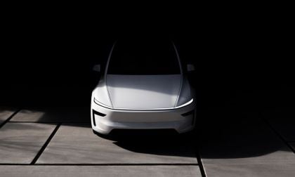 A sleek, modern white Tesla Model Y Juniper is illuminated against a dark background. The front view highlights its aerodynamic design and minimalistic style. Shadows create a dramatic, futuristic tone.