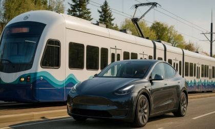 Tesla Model Y driving next to an electric light rail train