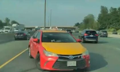 A red and yellow Toyota taxi labeled "co-op" is spun out on a multi-lane highway. Surrounding cars and lush trees line the road under a clear sky.