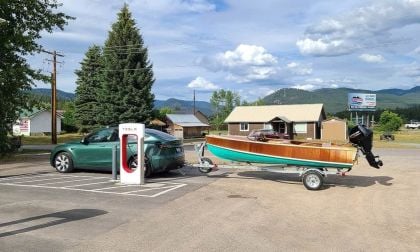 Green Tesla Model Y towing a classic wooden boat