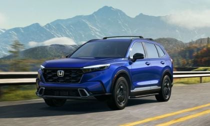 A blue 2025 Honda CR-V drives on a highway with mountains in the background under a clear sky. The scene conveys a sense of adventure and freedom.