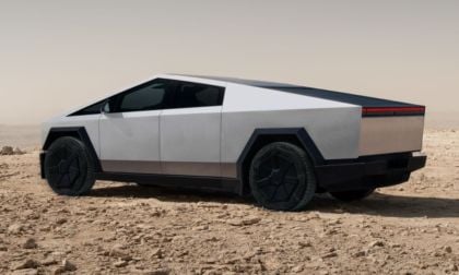 Futuristic looking silver Tesla Cybertruck with angular design and dark windows on a rocky desert landscape. The vehicle conveys a sleek, modern, and rugged tone.