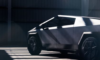 Futuristic, angular Tesla Cybertruck in dimly lit garage. Sunlight casts geometric shadows, highlighting sleek, metallic design. Modern and innovative ambiance.