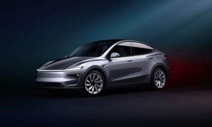 Lustrous silver Tesla Model Y in a dimly lit studio, showcasing its aerodynamic design and modern features, against a gradient blue and red background.