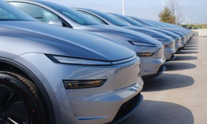 A row of silver Tesla Model Y's parked in a lot, showcasing their aerodynamic design and glossy finish under clear blue skies.