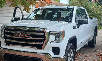 White 2021 GMC 1500 parked in a driveway surrounded by fall foliage. The driver's door is open, conveying readiness and adventure.