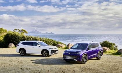 Two modern 2025 Volkswagen Tayrons, a white one and a purple one, parked by the seaside with a scenic view of mountains and clouds in the background.
