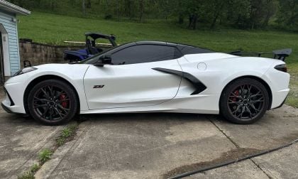 A sleek white Corvette Z06 parked on a driveway, showcasing its aerodynamic design and black alloy wheels against a green backdrop.
