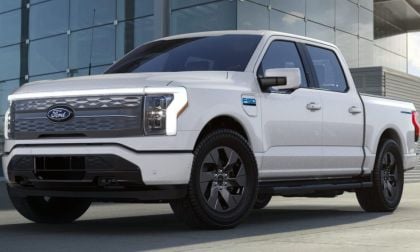 A white Ford F-150 Lightning truck parked in front of a modern building, showcasing its sleek design and prominent grille.